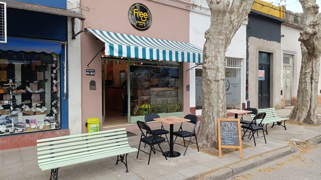 Frente de Free Crepes en Belgrano 94 bis: toldo a rayas, cartel Free, mesas, sillas y bancos en la vereda